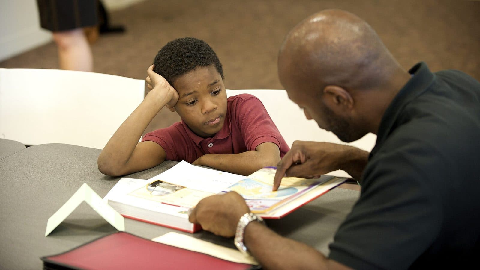 A tutor pointing to a workbook while a student follows along